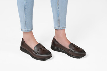 Young woman with fair legs modeling comfortable brown leather loafers with tassels, paired with light blue skinny jeans, clean, white background, emphasizing casual elegance and comfort, everyday wear