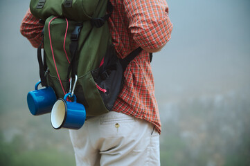 Hiker with backpack and camping gear standing in misty mountain landscape
