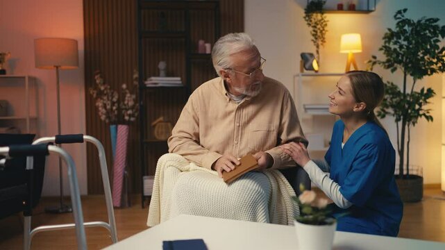 Caring female nurse talking with senior male reading a book, home care services
