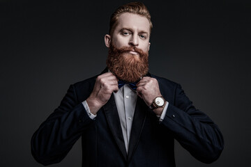 Fototapeta premium Male accessory. Gentleman in tuxedo bowtie has luxury watch. Expensive time wrist watch. Man in tuxedo adjusting bowtie and watch. Elegant watch accessory. Time. Elegant gentleman isolated on grey