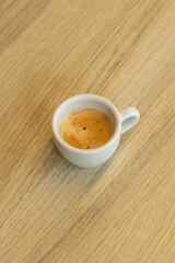 A single shot of freshly brewed espresso in a white cup sits on a wooden table. The creamy, aromatic coffee showcases a perfect crema, inviting coffee lovers to enjoy a cozy coffee break.