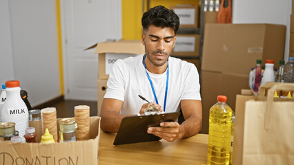 Hispanic man volunteers at indoor food donation center, organizing supplies and writing inventory.