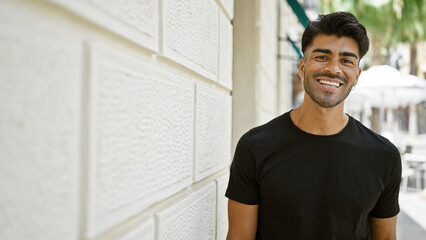 Handsome young hispanic man smiling gently on a sunlit city street, radiating positivity and style.