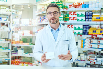 Man, portrait and pharmacist with box for symptoms, dosage or side effects of pharmaceutical product at pharmacy. Male person or medical employee explaining information on drugs at dispensary store