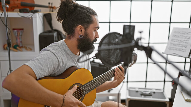 A young hispanic man with a beard practices guitar in a music studio, showcasing talent and focus.