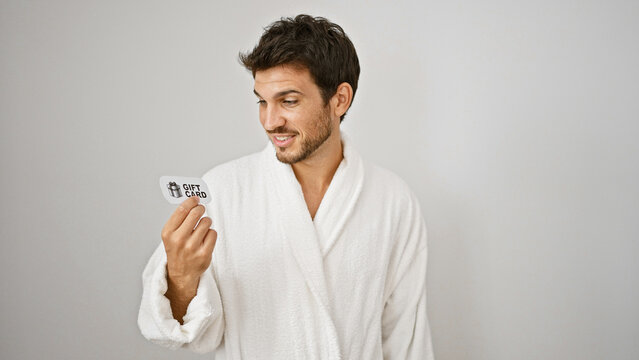 Handsome young man in white bathrobe admiring a gift card against isolated white background.