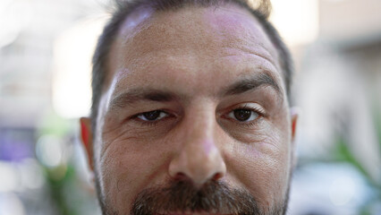 Close-up portrait of a mature hispanic man with grey hair, showing introspective eyes and an urban street in the blurry background.