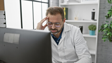 A mature hispanic man with grey hair in a lab coat appears stressed while working on a computer in...