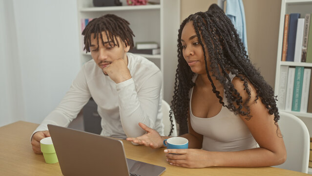 A man and woman engage in a conversation over a laptop in a modern living room, suggesting a casual business or personal planning setting. - Powered by Adobe