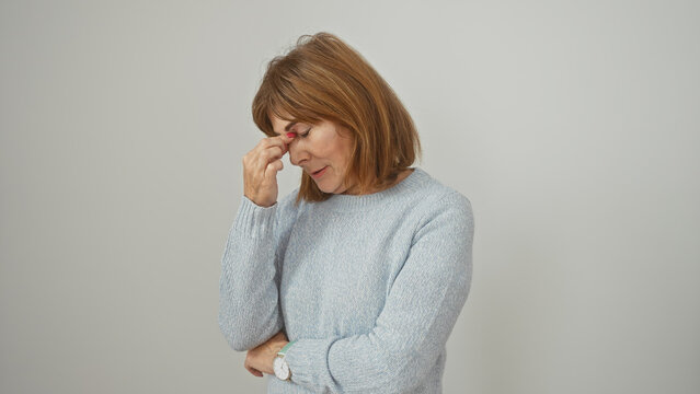Tired middle-aged woman in sweater rubbing eyes on white background