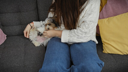 A young woman cuddles with her biewer yorkshire terrier on a sofa indoors, surrounded by colorful...