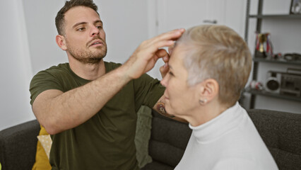 Fototapeta premium A man gently touches the head of a concerned-looking woman while they sit on a couch in a cozy living room, portraying intimacy and care.