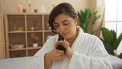 Young woman in spa room examining hair ends in a wellness center with indoor plants and shelves behind her