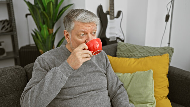 A senior man relaxing with a red mug in a modern living room, exuding coziness and domestic lifestyle.