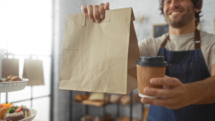 Young man in bakery holding a paper bag and coffee cup with pastries displayed in the background