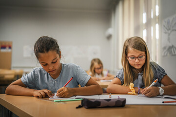 Young girl students do tasks and write on notebook on the class