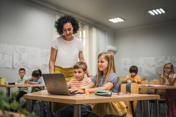 Mature teacher teach boy and girl students how to use laptop