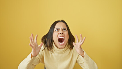 Angry young woman shouting against a yellow background, expressing frustration and emotion.