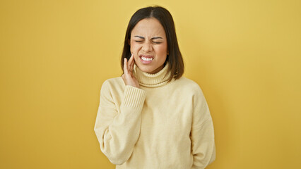 Fototapeta premium A young hispanic woman grimaces in pain isolated against a yellow background, embodying discomfort and beauty.