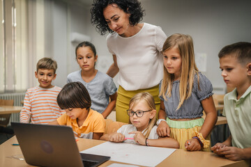 Fototapeta premium Mature teacher teach her students how to use laptop in the classroom