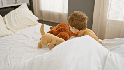 A blond toddler boy plays with plush toys in a bright bedroom, depicting innocence and childhood at...