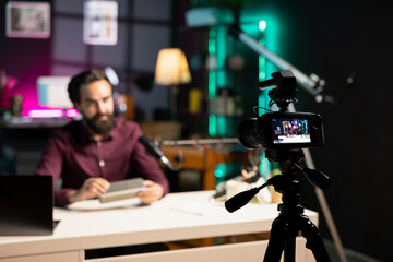 Focus on tech guru in blurry background doing technology review of wireless portable speaker. Close...