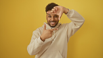 Cheerful man framing face with fingers against yellow background