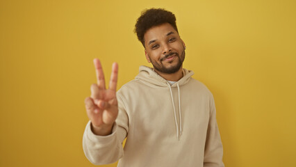 Naklejka premium Handsome black man making peace sign in beige hoodie against yellow background