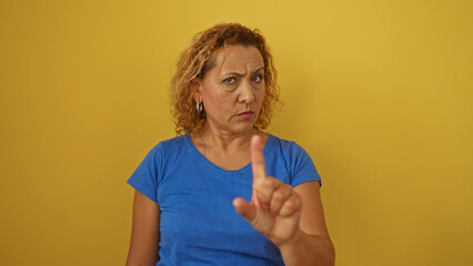 Hispanic woman with curly hair gestures seriously against an isolated yellow background.