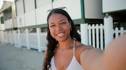 Young hispanic female with swimwear talking on avideo call on her summer vacation. Brazilian woman having fun and smiling streaming online and looking at camera wearing bikini swimsuit on a shore - Powered by Adobe