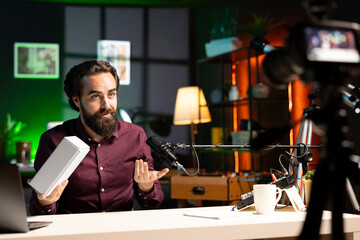 Tech influencer using professional camera and mic to film technology review of smartphone, doing unboxing video. Man showing phone box to viewers, recording with high tech devices