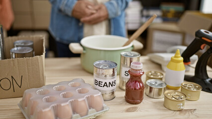 Middle-aged man preparing emergency supplies with canned food, desk, indoor, storage, unrecognizable, food, container, preparedness, safety, man.