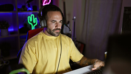 Handsome hispanic man with beard wearing headphones in a dark gaming room at night