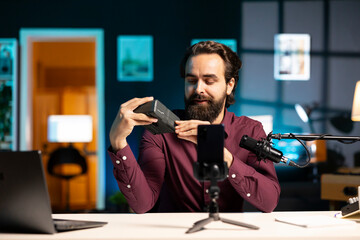 Tech expert presenting features of newly launched V mount battery, filming technology review using smartphone on tripod. Reviewer showcasing charging device specs, recording with phone