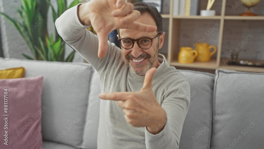 Poster a cheerful middle-aged man with a beard making a frame with his hands in a cozy living room interior