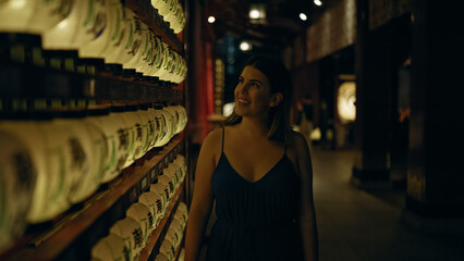 Fototapeta premium Beautiful young hispanic woman looking at asian lantern at japanese temple in tokyo at night