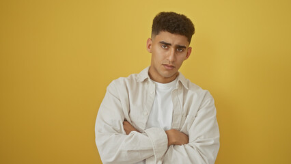 Handsome young man with arms crossed standing against a yellow background, exuding a confident aura.