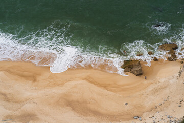 A lonely elderly man walks on the sandy beach of Nazare in Portugal, photo from above.