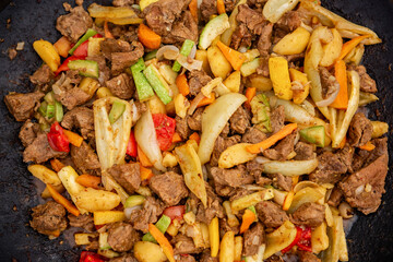 Close-up of a vibrant stir-fry dish featuring juicy beef chunks and fresh vegetables like bell peppers, onions, carrots, and zucchini, cooked to perfection.