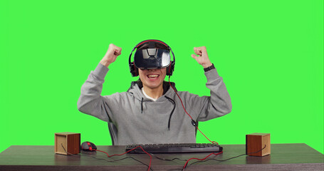 POV of player enjoying vr video games sitting at his desk over greenscreen backdrop, playing web based with friends and having fun with rpg gameplay. Man using virtual reality headgear.