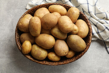 Many fresh potatoes in wicker basket on grey table, top view