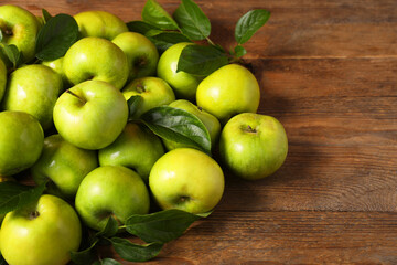 Ripe green apples with leaves on wooden table. Space for text