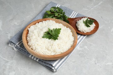 Tasty cooked rice in bowl with parsley and spoon on grey marble table