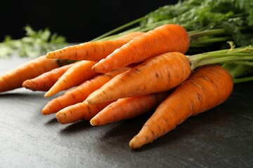 Tasty ripe juicy carrots on dark gray textured table, closeup