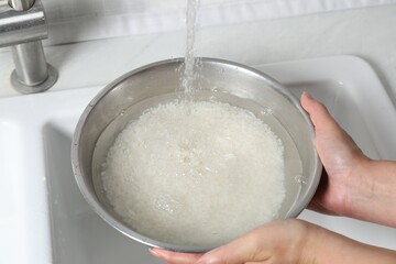 Woman rinsing rice in bowl above sink, closeup