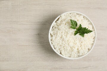 Delicious boiled rice in bowl and parsley on wooden table, top view. Space for text