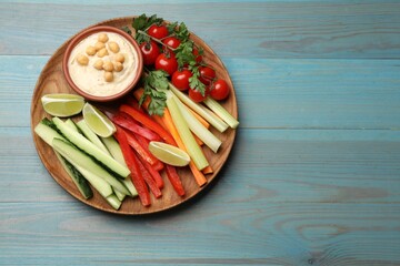 Tasty homemade hummus served with different vegetables on light blue wooden table, top view. Space for text