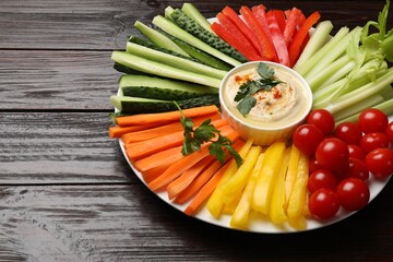 Tasty homemade hummus and different vegetables on dark wooden table