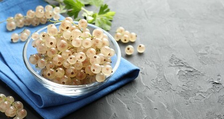 Fresh white currant berries in bowl and green leaves on gray textured table, closeup. Space for text