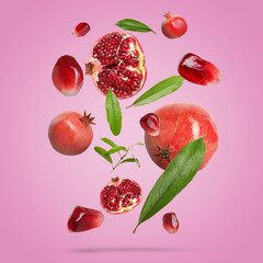 Fresh pomegranates, seeds and leaves in air on pink background